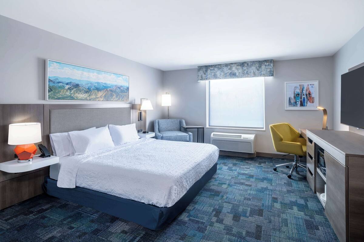 A hotel room with a bed, desk, chair, and artwork on the walls.