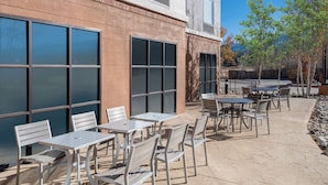 An outdoor patio with tables and chairs, large windows, and a building facade.