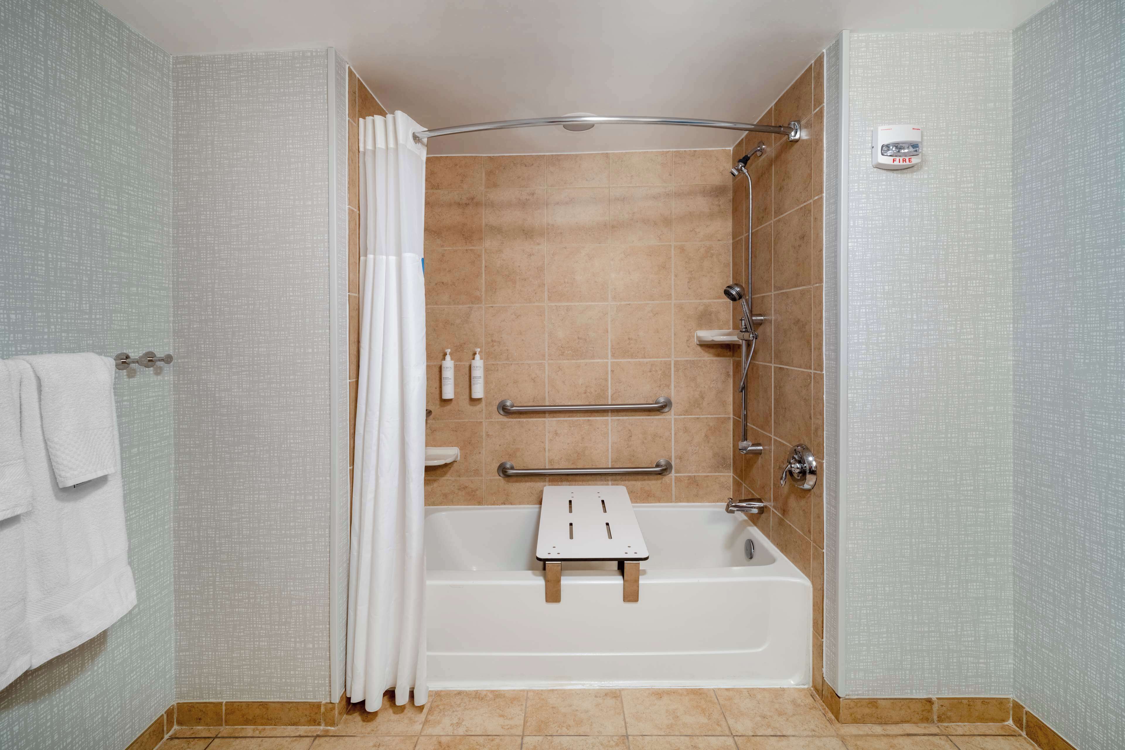 Een moderne badkamer met een douche, een bad met een handgreep en een handdoekhouder.