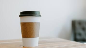Una taza alta y cilíndrica con tapa negra y base blanca, sobre una superficie de madera.