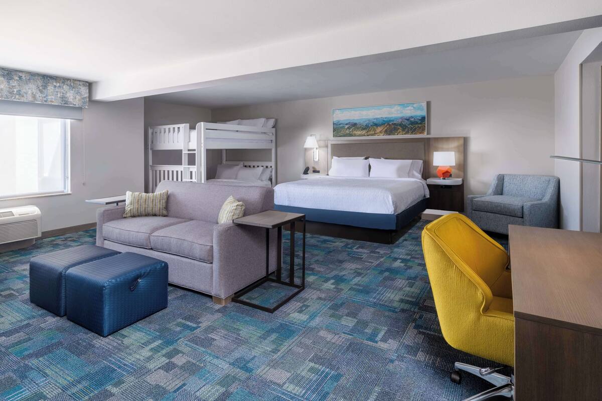 A hotel room with a bunk bed, a sofa, a desk, and a chair.