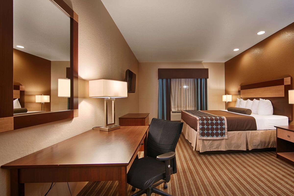 Ein Hotelzimmer mit Bett, Schreibtisch, Stuhl und zwei Nachttischen mit Lampen.