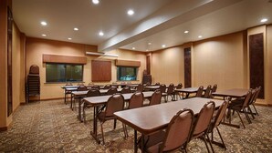 Un salón de conferencias con varias mesas y sillas, piso alfombrado y luces empotradas en el techo.