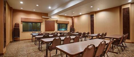 A conference room with multiple tables and chairs, carpeted floor, and recessed ceiling lights.