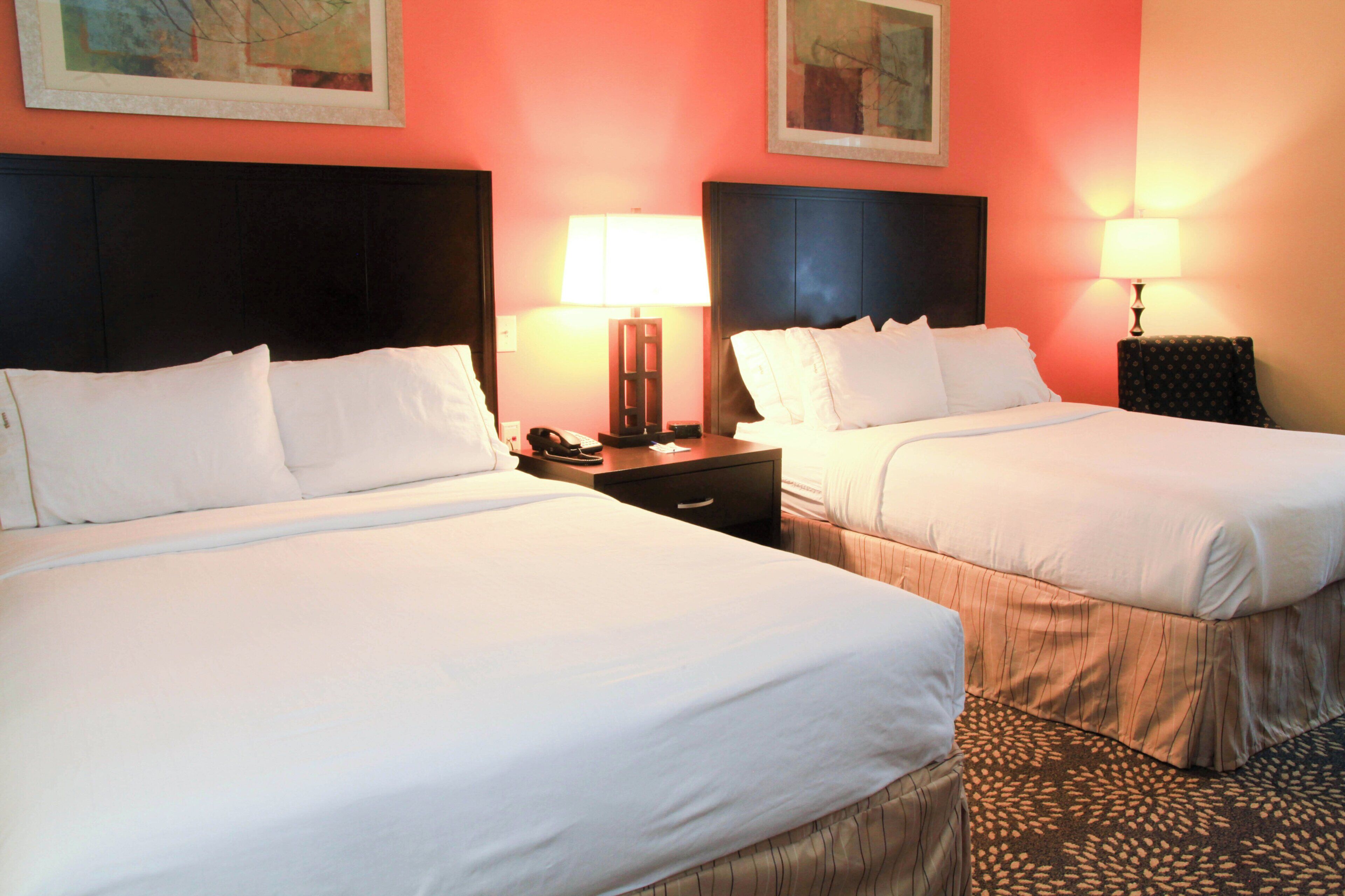 A hotel room with two beds, nightstands with lamps, and artwork on the walls.