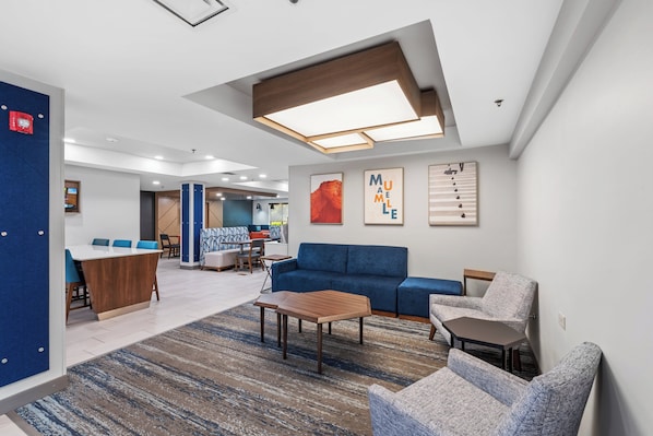 A modern lounge area with a blue sofa, a wooden coffee table, and a patterned rug.