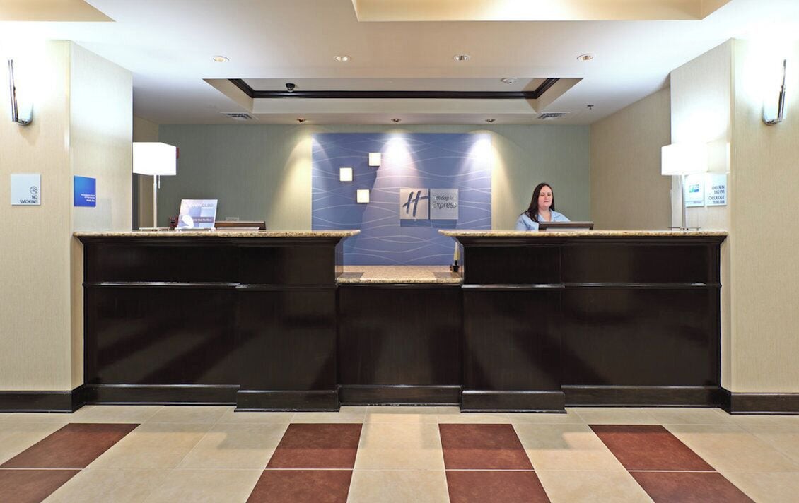 A hotel reception area with a reception desk, a receptionist, and a wall with a logo.