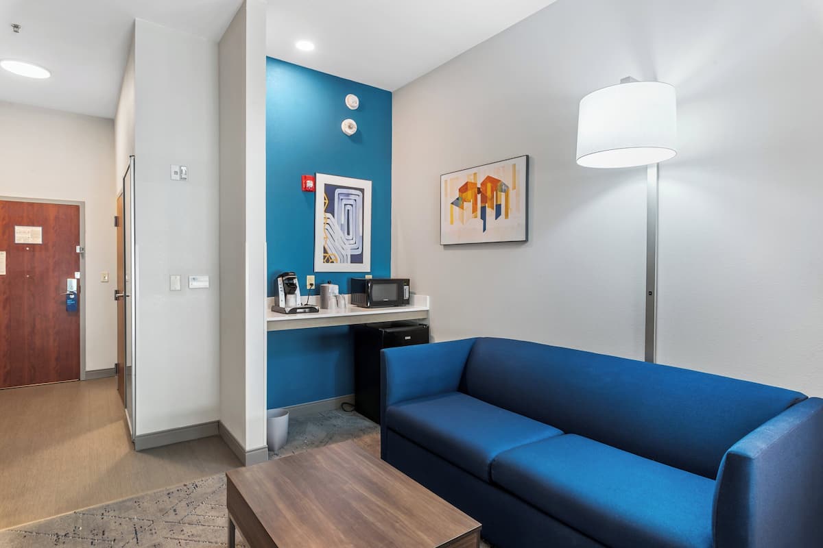 Une chambre d’hôtel moderne avec un canapé bleu, une table basse en bois, un four à micro-ondes et une petite kitchenette.
