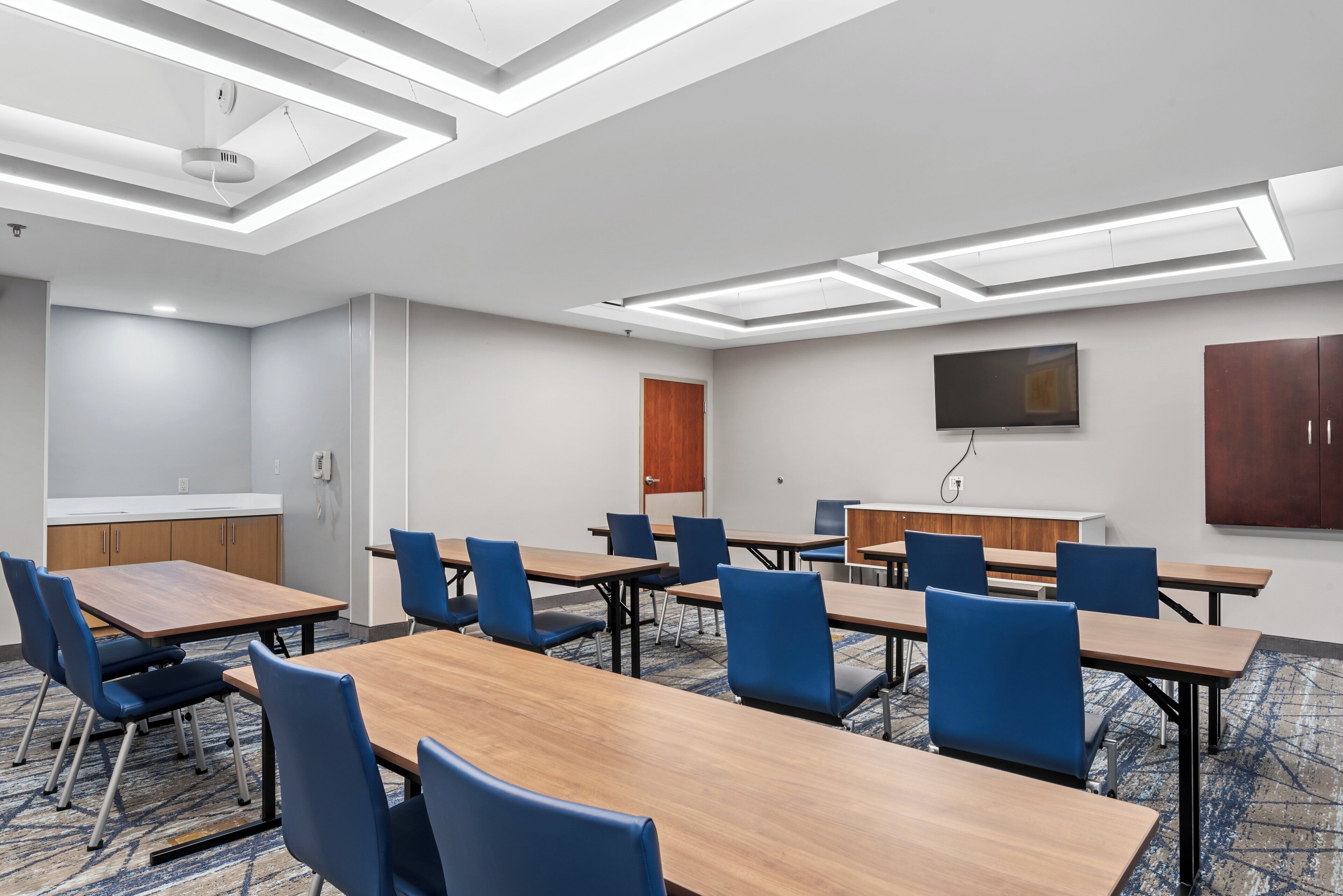 A conference room with multiple tables and chairs, a flat-screen TV, and a wooden cabinet.