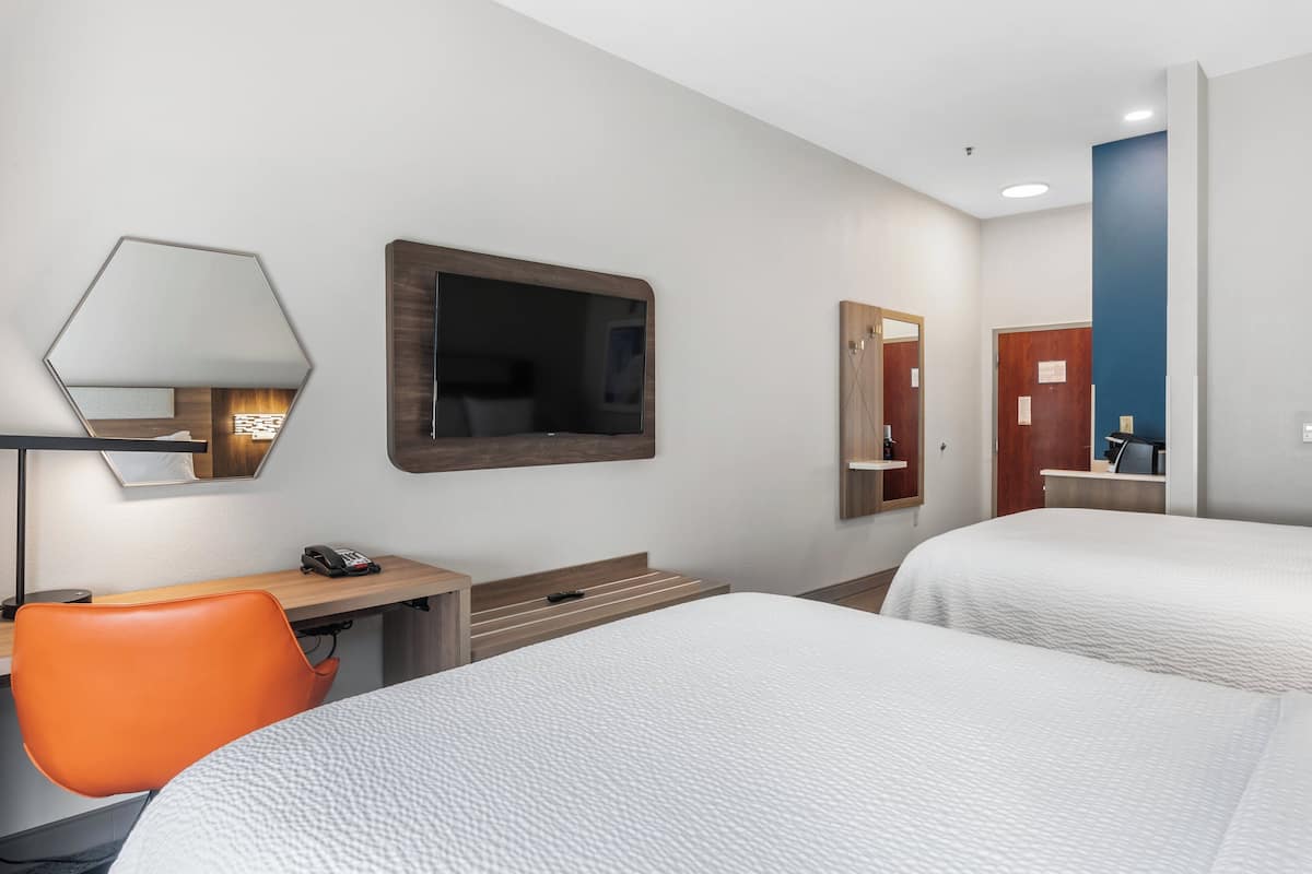 Une chambre d’hôtel avec deux lits, un bureau, une chaise orange, une télévision et un miroir.
