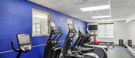 Ett gym med träningsutrustning, ett stort fönster och en blå vägg.