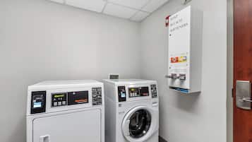 A laundry room with two front-loading washing machines and a wall-mounted soap and bleach dispenser.