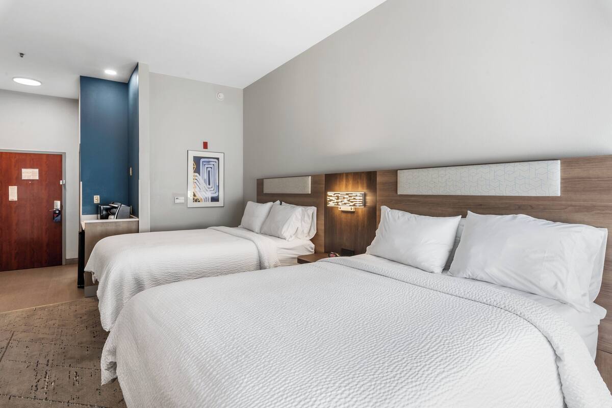 Une chambre d’hôtel avec deux lits, une tête de lit en bois, une petite table de chevet et une œuvre d’art accrochée au mur.