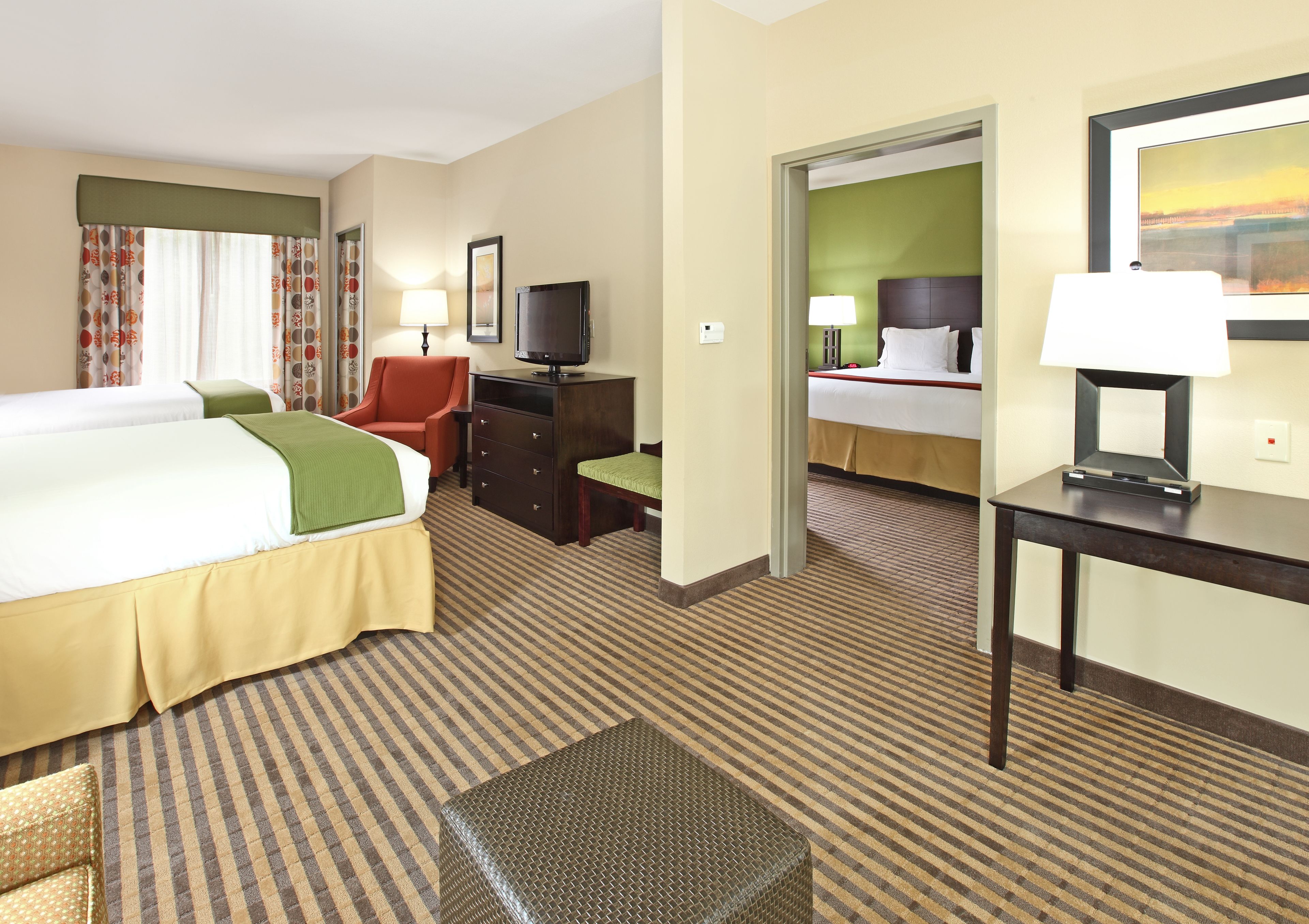 Quarto de hotel com cama, escrivaninha, cadeira, televisão e luminária.