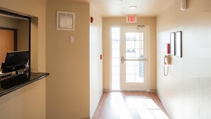 A hallway with a computer monitor, an exit sign, and a phone on the wall. - WoodSpring Suites Colonial Heights Fort Lee (Colonial Heights)