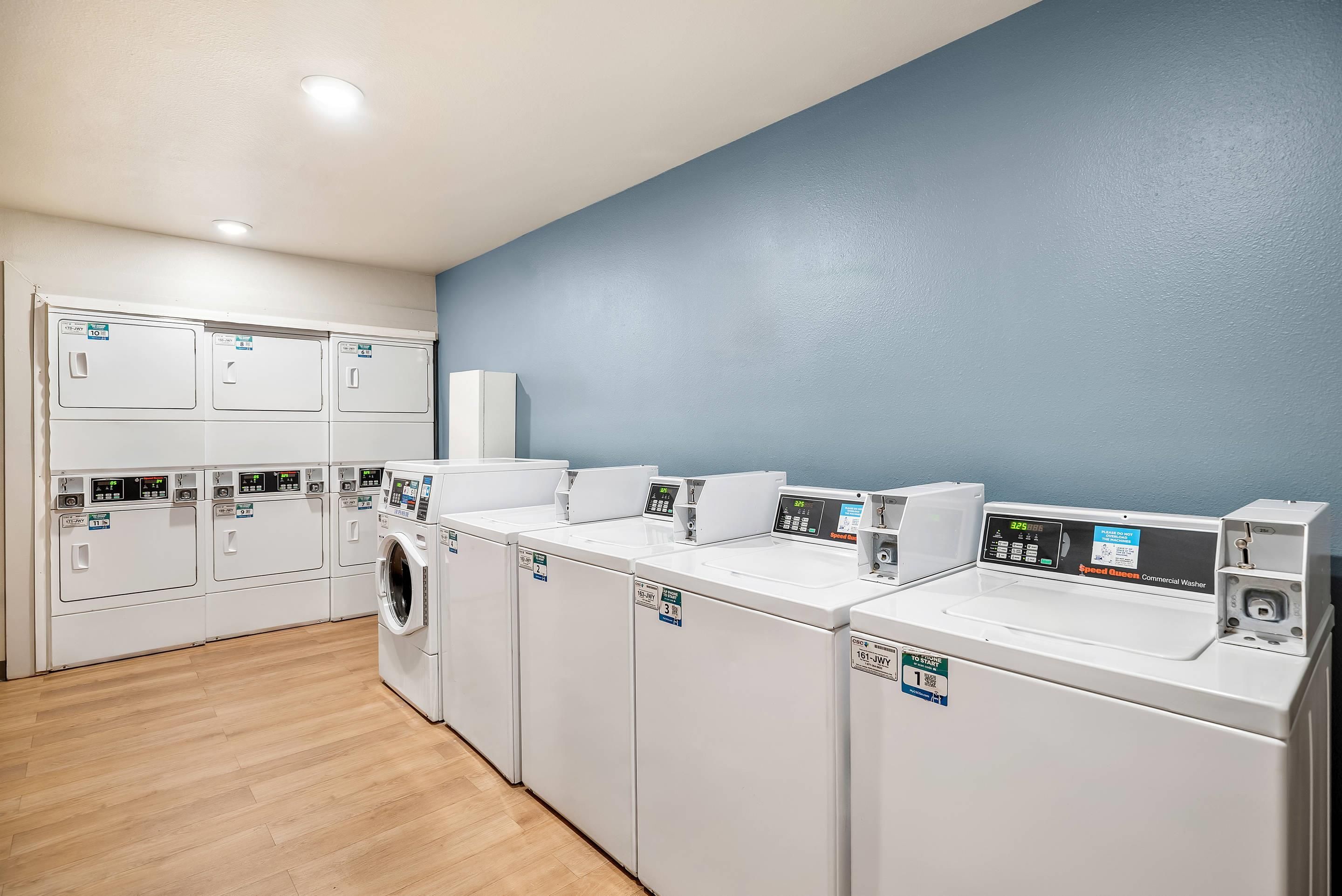 A laundry facility with multiple washing machines and dryers, wooden flooring, and a blue wall.