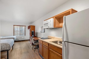 Cocina compacta con refrigerador, microondas y estufa. Hay una mesa de comedor con sillas y una ventana con persianas.