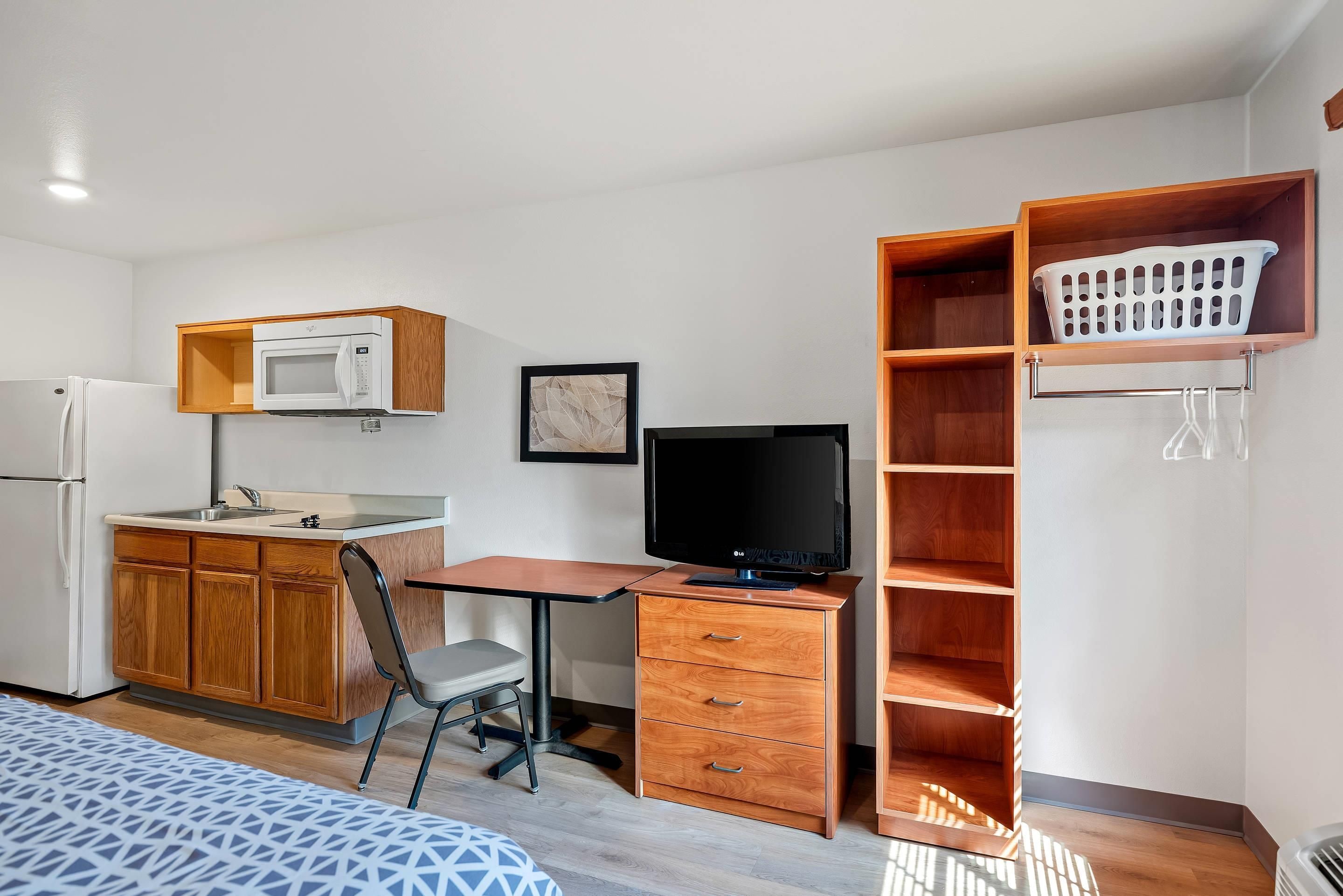 Habitación compacta con kitchenette, un escritorio con ordenador, una silla y una cama.