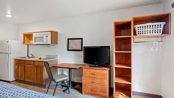 Habitación compacta con kitchenette, un escritorio con ordenador, una silla y una cama.