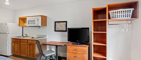 Habitación compacta con kitchenette, un escritorio con ordenador, una silla y una cama.