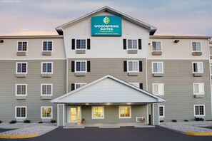 A multi-story hotel with a prominent sign for Woodspring Suites, featuring a modern design with a flat roof and a covered entrance. - WoodSpring Suites Colonial Heights Fort Lee (Colonial Heights)