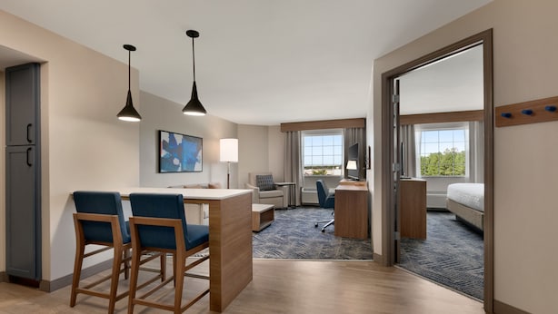 Hotelkamer met kitchenette, een eethoek met twee barkrukken, een bureau met stoel, een bed en een groot raam met uitzicht.