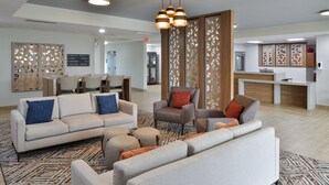 Een moderne hotellobby met een receptiebalie, een zithoek met banken en stoelen, en decoratieve houten panelen.