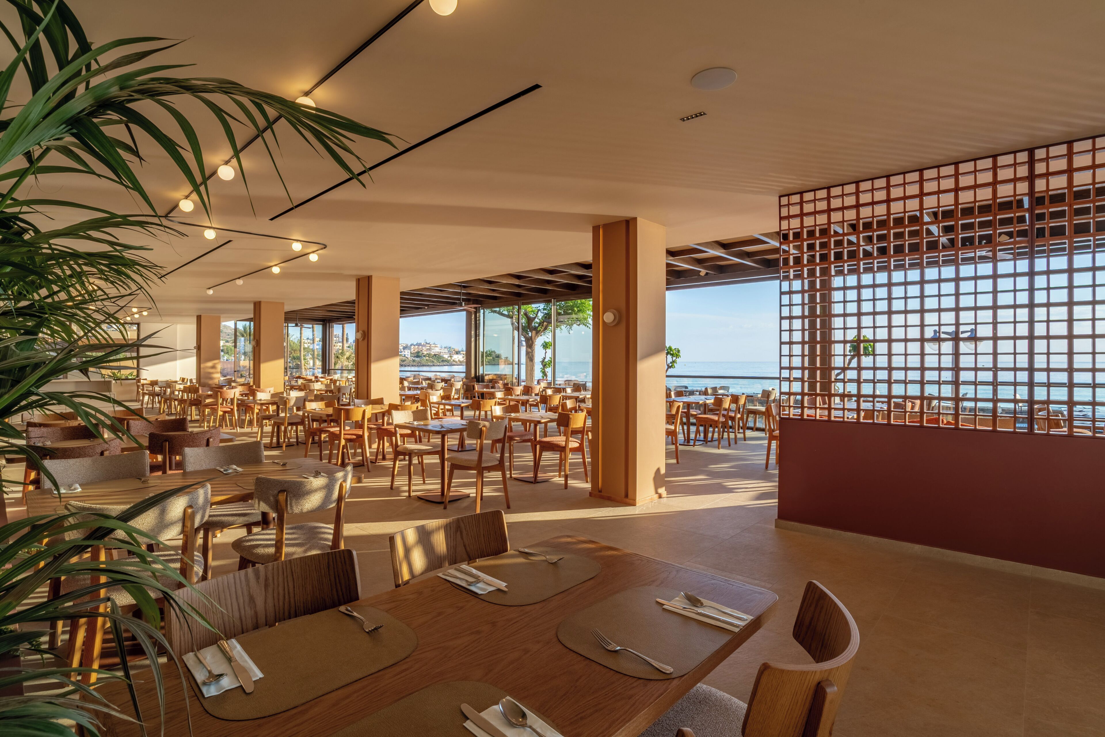 A spacious outdoor dining area with tables and chairs, large windows, and a view of the sea.