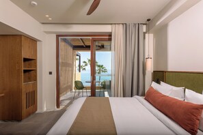 Une chambre d’hôtel avec un lit, une armoire en bois, un balcon donnant sur la mer et une table avec des chaises.
