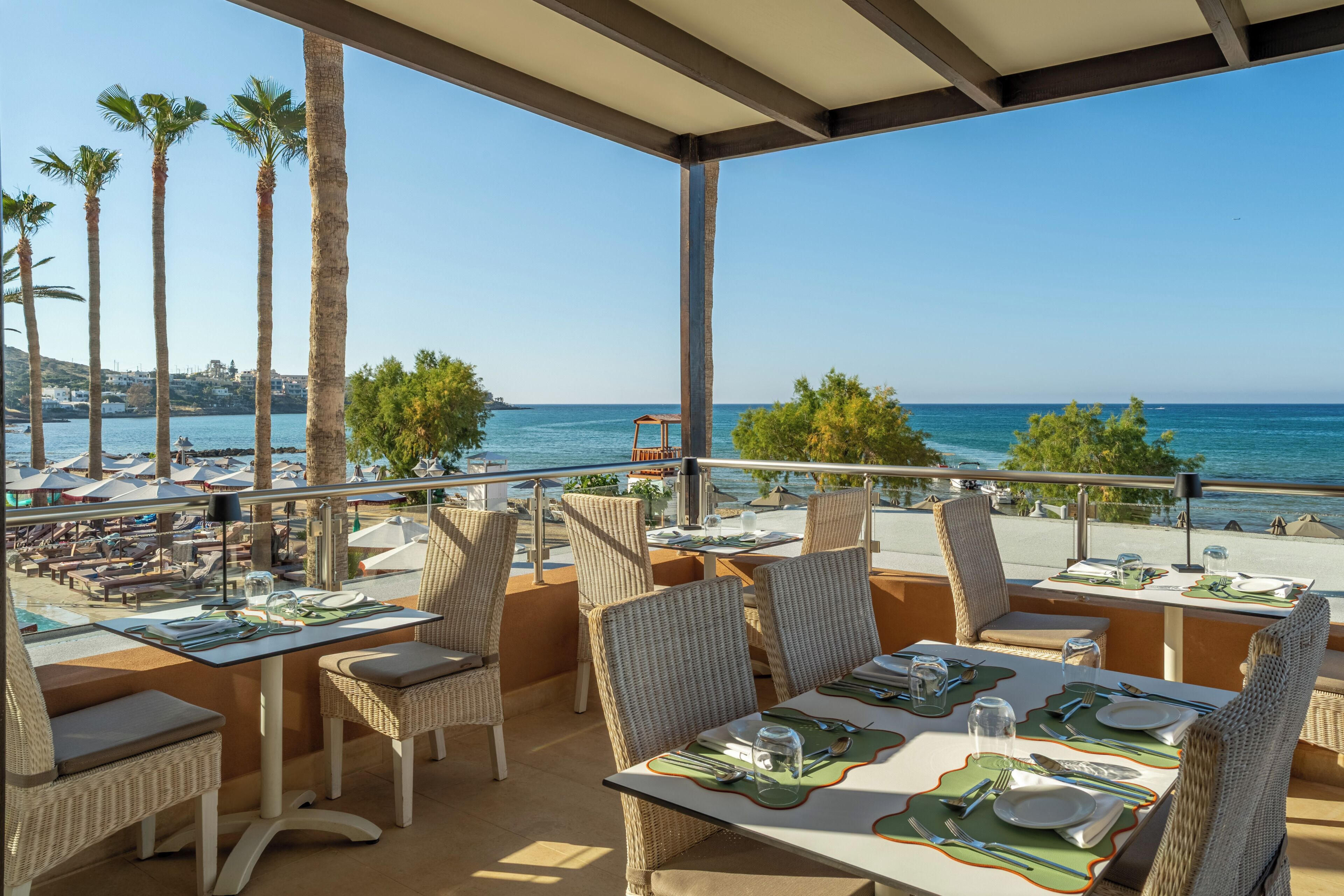 Un espacio para comer al aire libre con mesas y sillas, con vista a una playa y el mar.