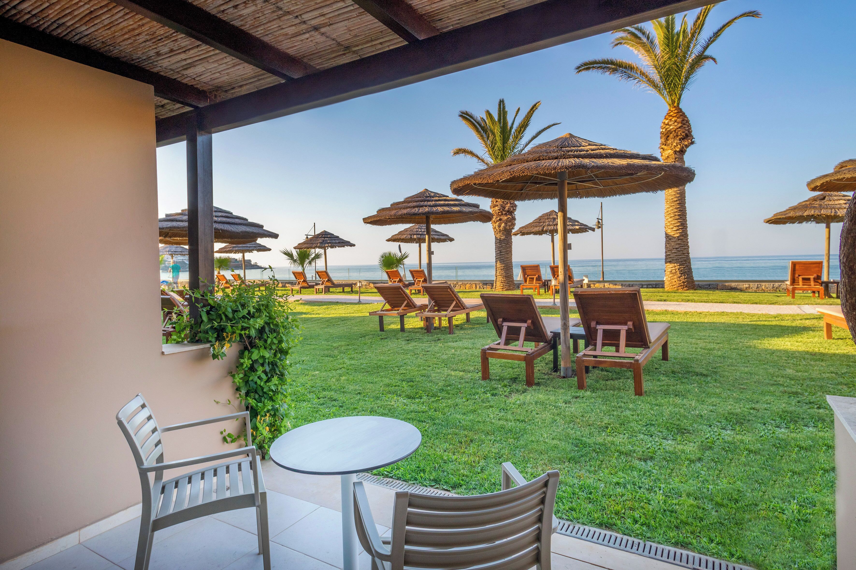 Un espacio al aire libre cubierto con sillas y mesas, palmeras y vista a la playa.