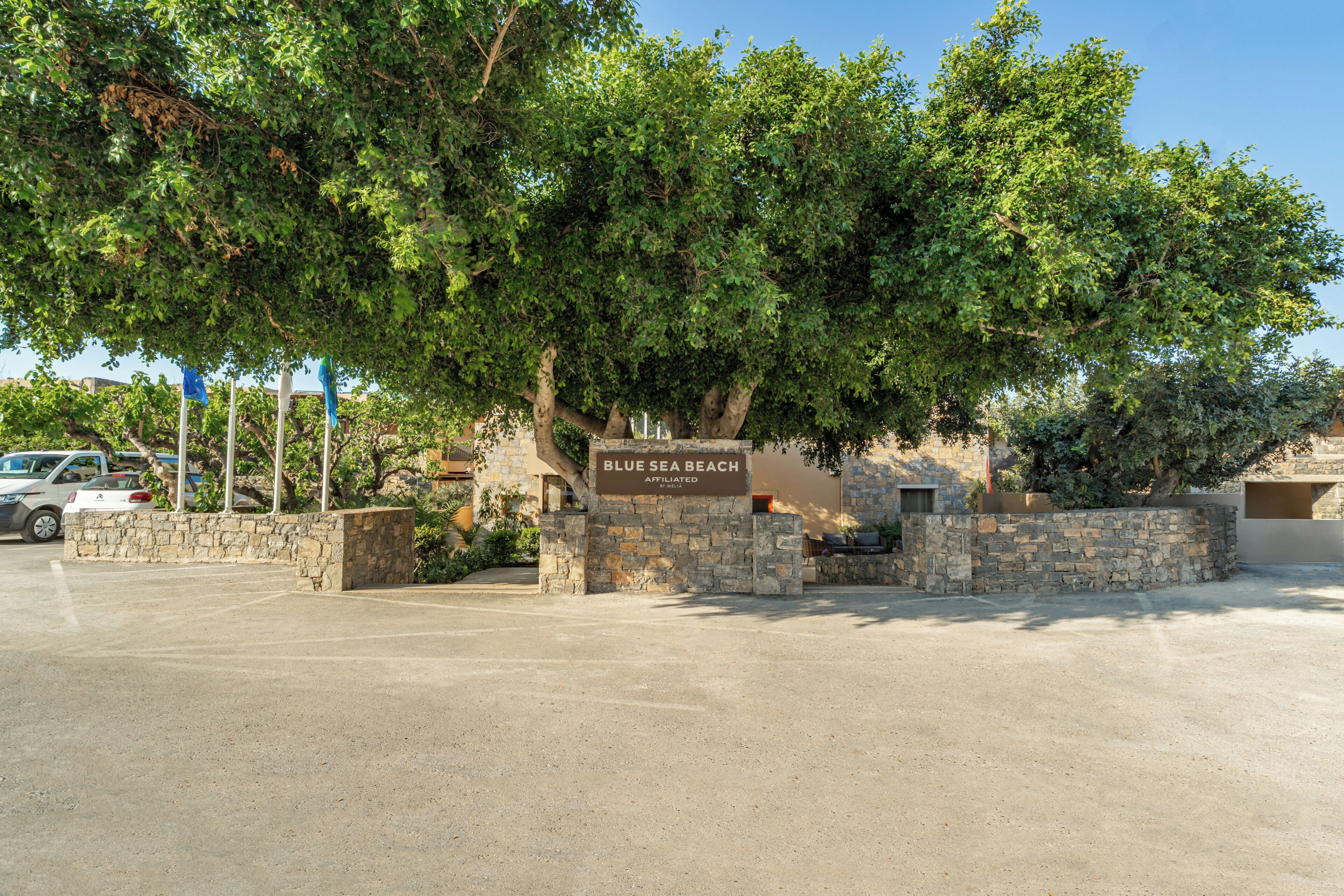 A sign for 'Blue Sea Beach' with a stone wall and trees in the background.