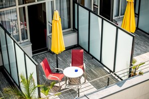 A modern outdoor seating area with a glass partition, red chairs, a white table, and yellow umbrellas.