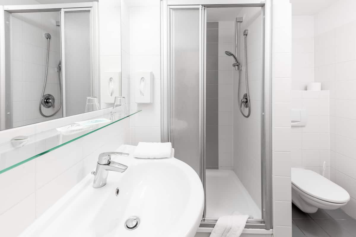 Casa de banho moderna com cabine de duche em vidro, lavatório branco com prateleira em vidro e sanita.