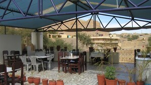 Een terras buiten met tafels en stoelen, plantenbakken en een uitzicht op de omliggende gebouwen.