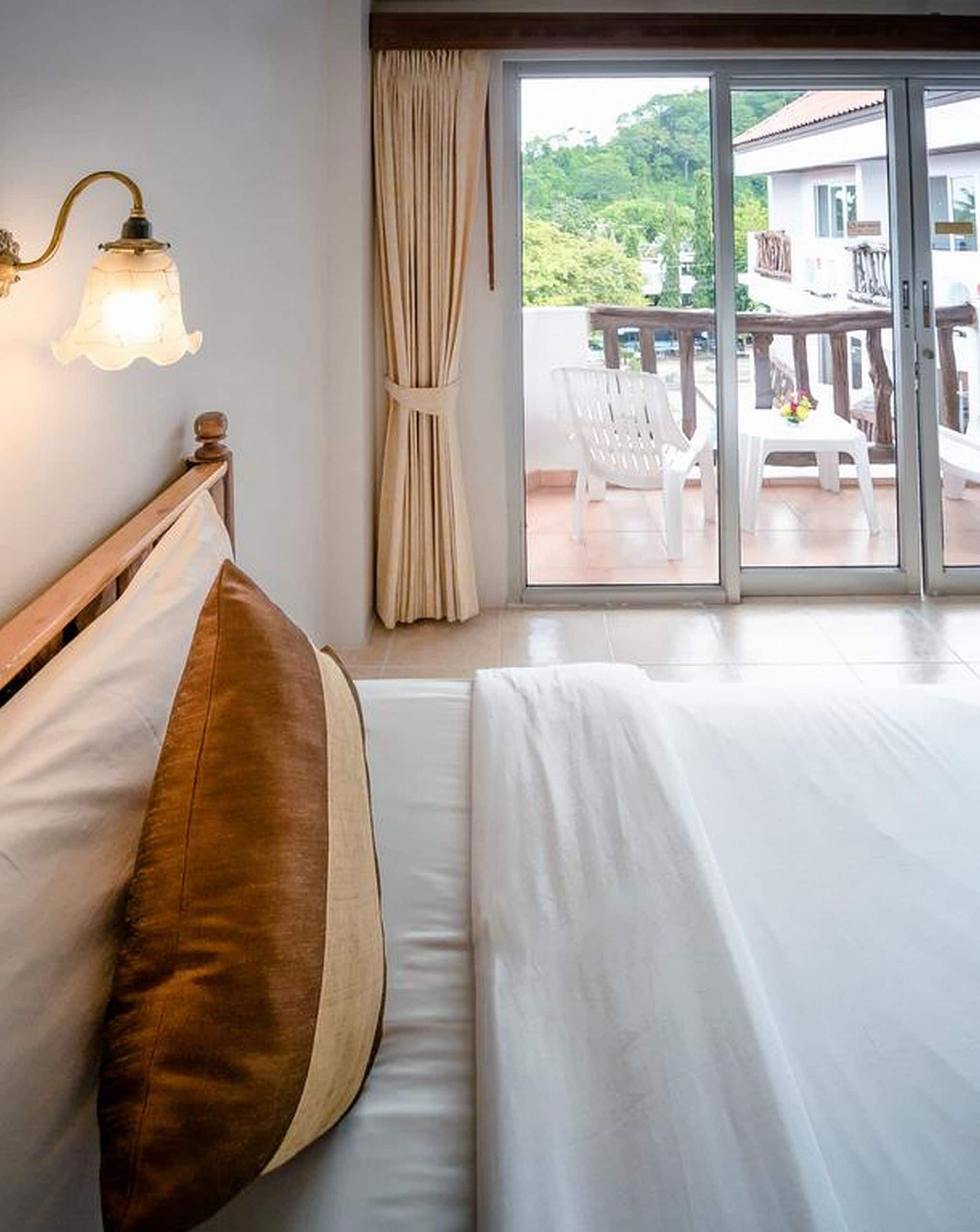 Une chambre d’hôtel comprenant un lit, une table de chevet, une lampe fixée au mur et une porte-fenêtre coulissante donnant sur un espace extérieur aménagé.