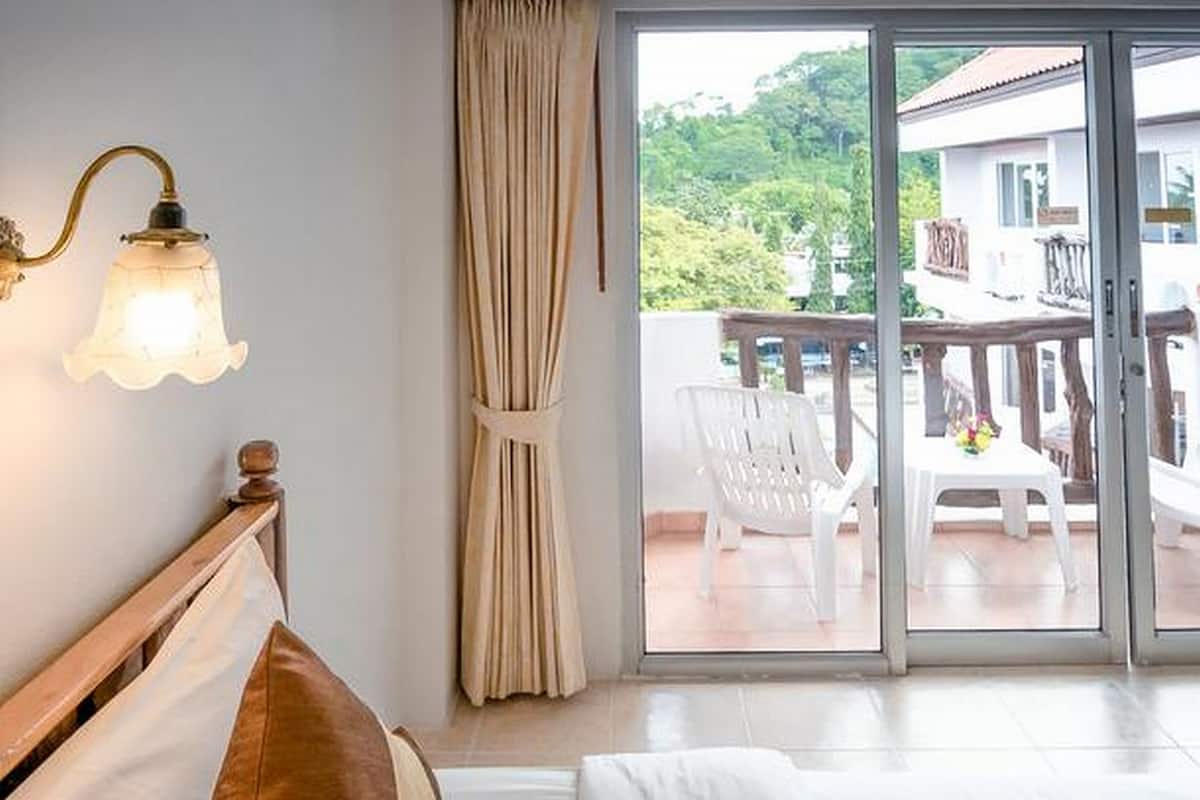 A hotel room with a bed, a nightstand, a wall-mounted lamp, a sliding glass door leading to an outdoor seating area.