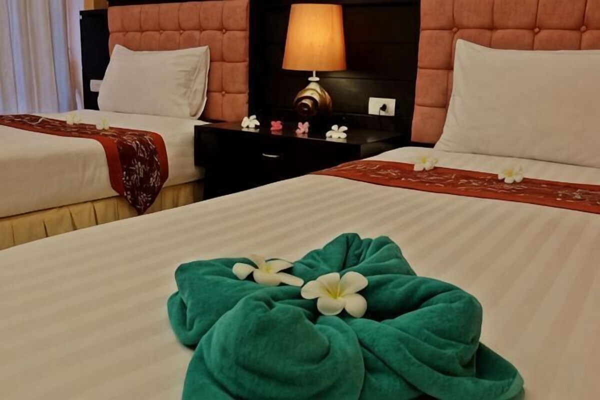 A hotel room with two beds, a nightstand with a lamp, and a floral arrangement on the bed.