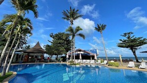 A clear blue pool surrounded by palm trees and lounge chairs, with a building and a view of the ocean in the background. - Andaman Lanta Resort (Ko Lanta)