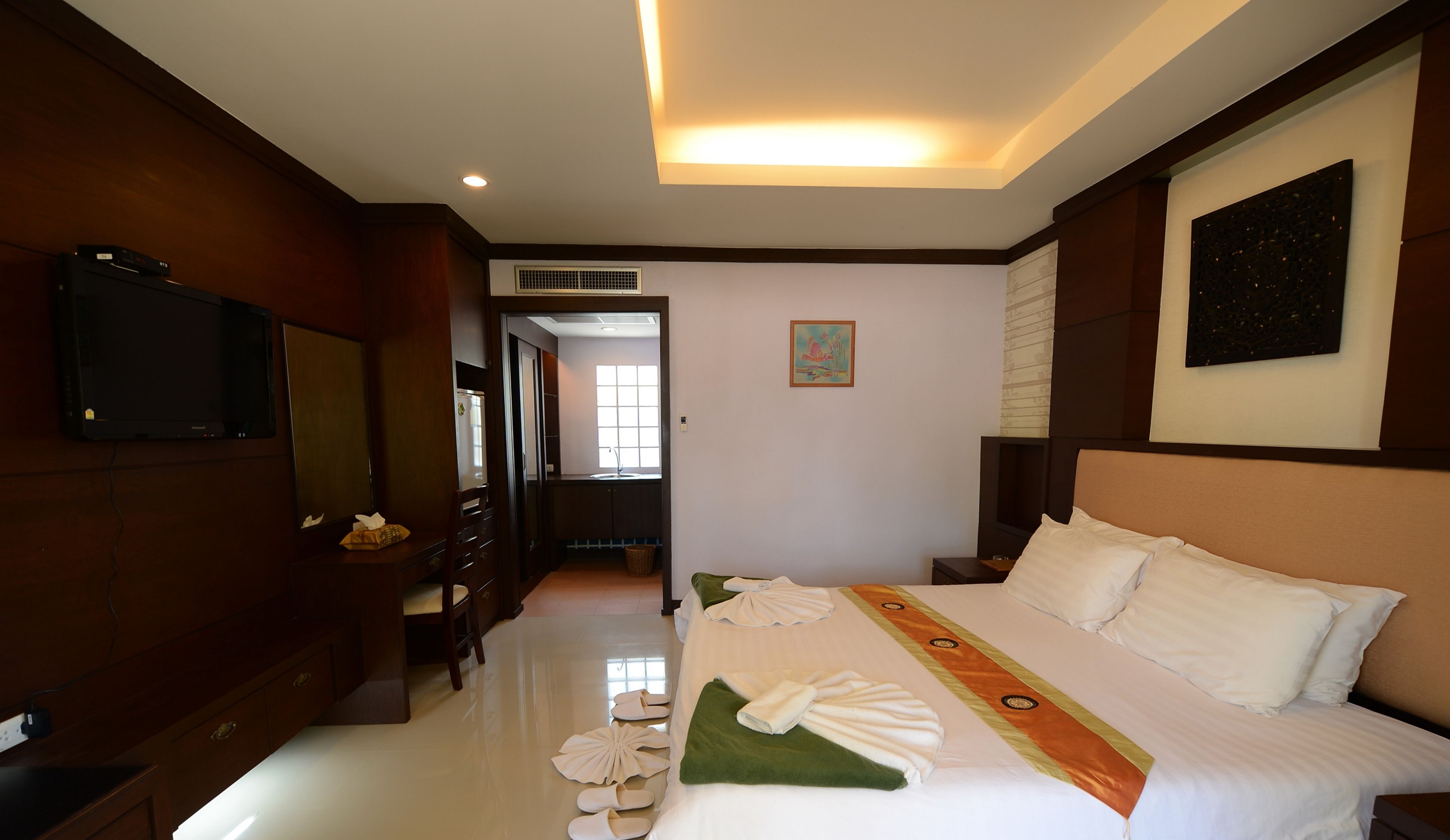 A hotel room with a large bed, a TV mounted on the wall, a desk with a chair, and a bathroom visible through an open door.