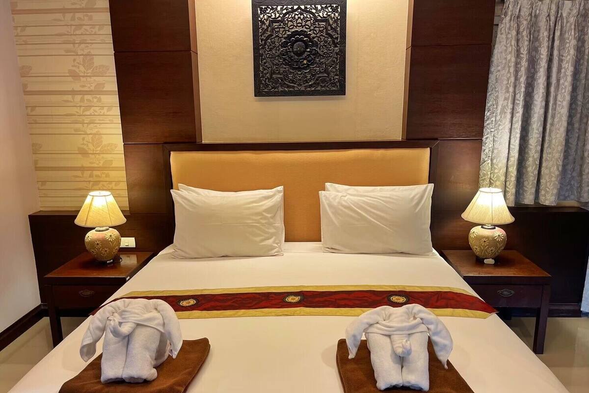 Quarto de hotel com uma cama grande, duas almofadas, duas mesas de cabeceira com luminárias e duas toalhas dobradas na cama.