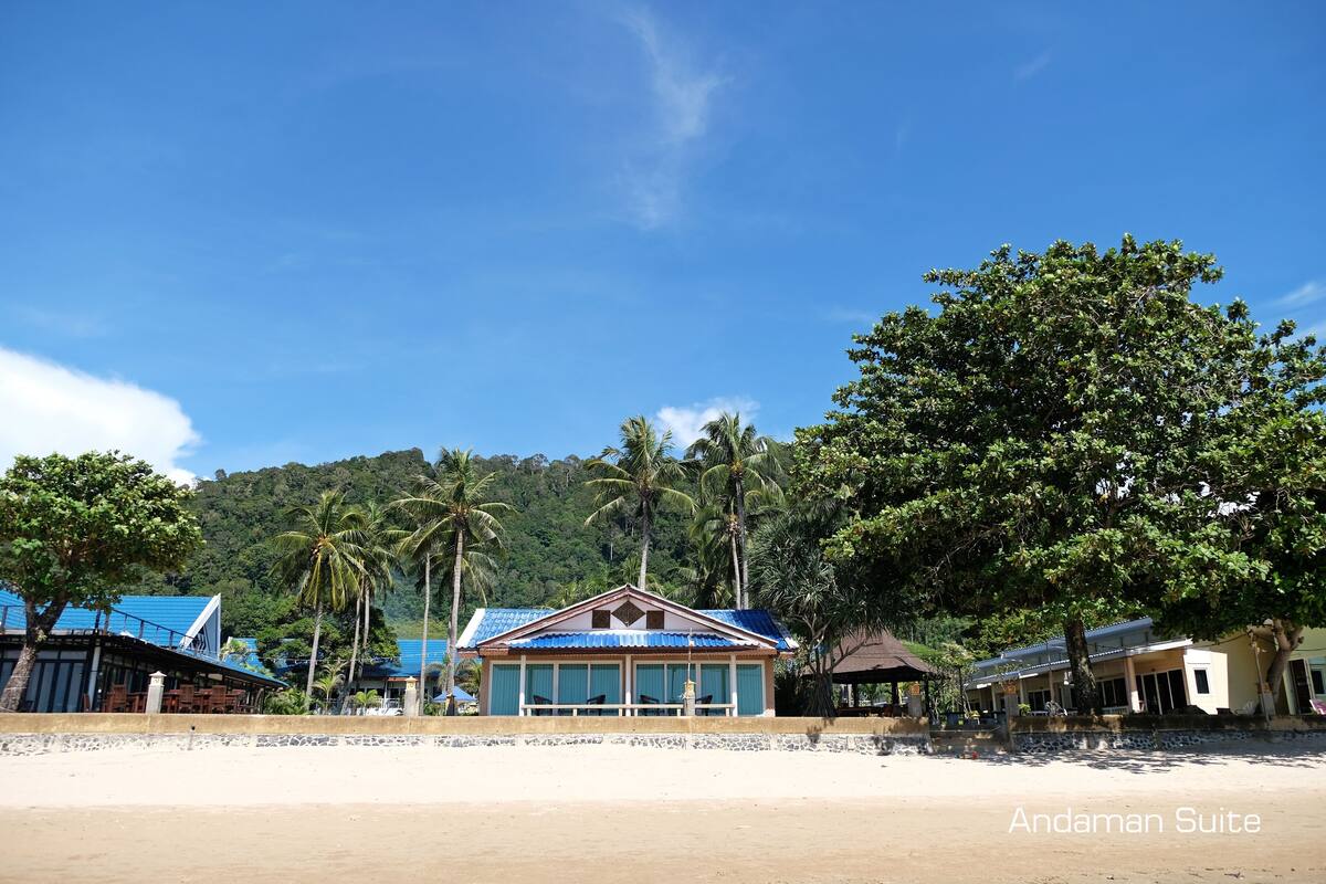 Hotel na praia com telhado azul, palmeiras e céu claro.
