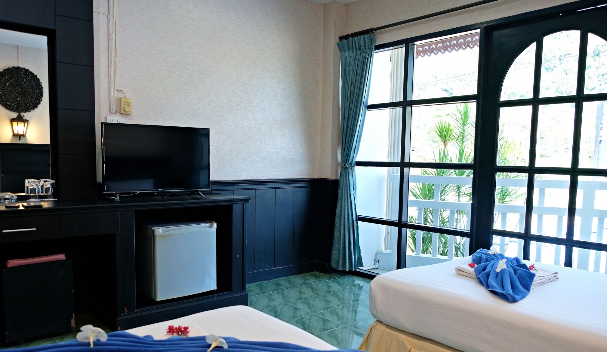 Une chambre d’hôtel avec un lit, une télévision, un petit réfrigérateur, un miroir et une fenêtre avec des rideaux.