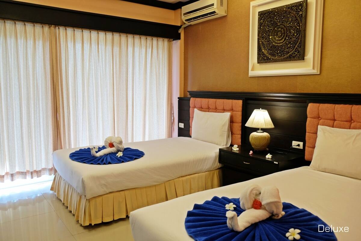 Quarto de hotel com duas camas, uma mesa de cabeceira com abajur e um objeto decorativo na parede.