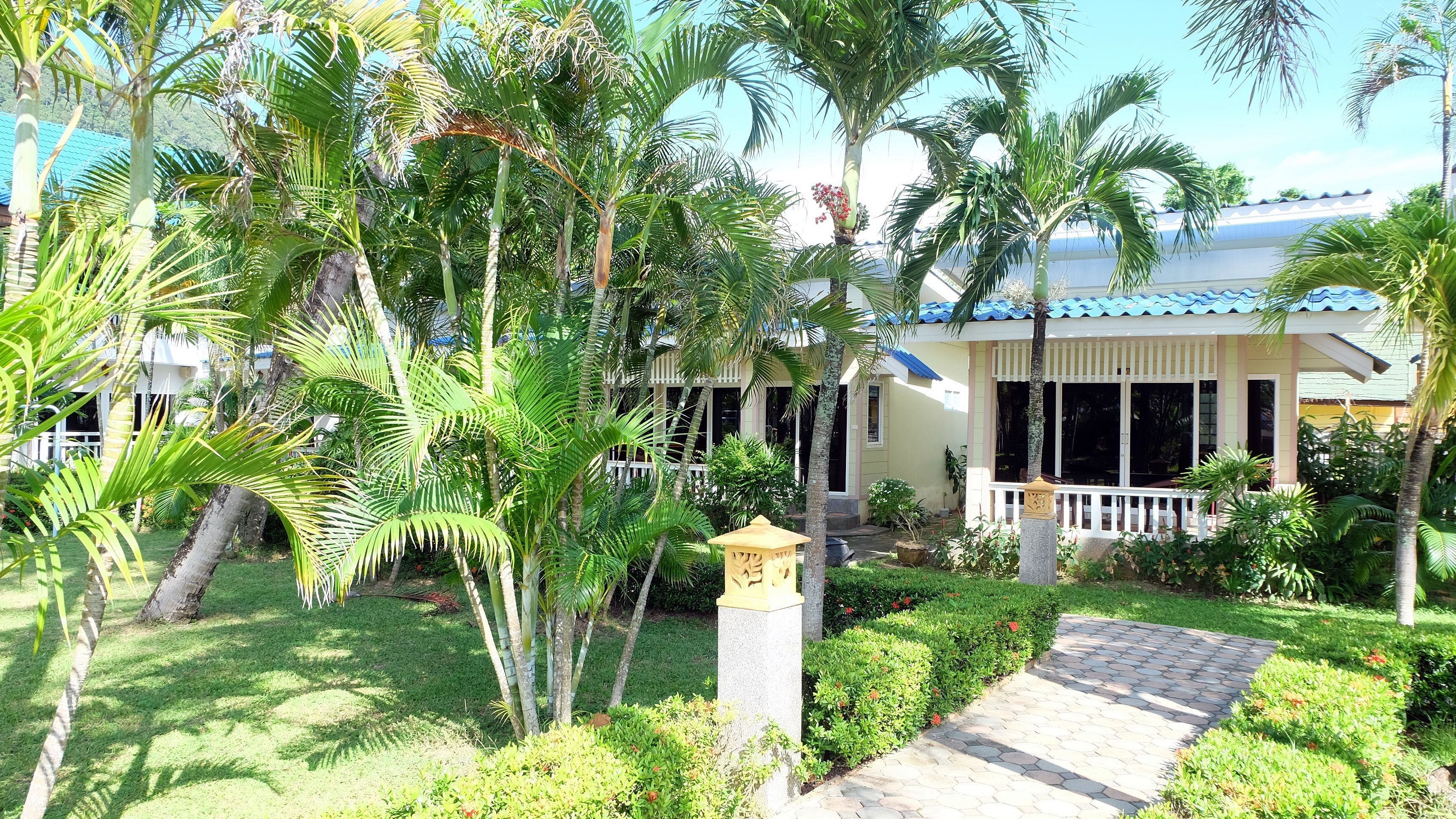 A tropical resort with a paved pathway, palm trees, and a building with a blue roof.