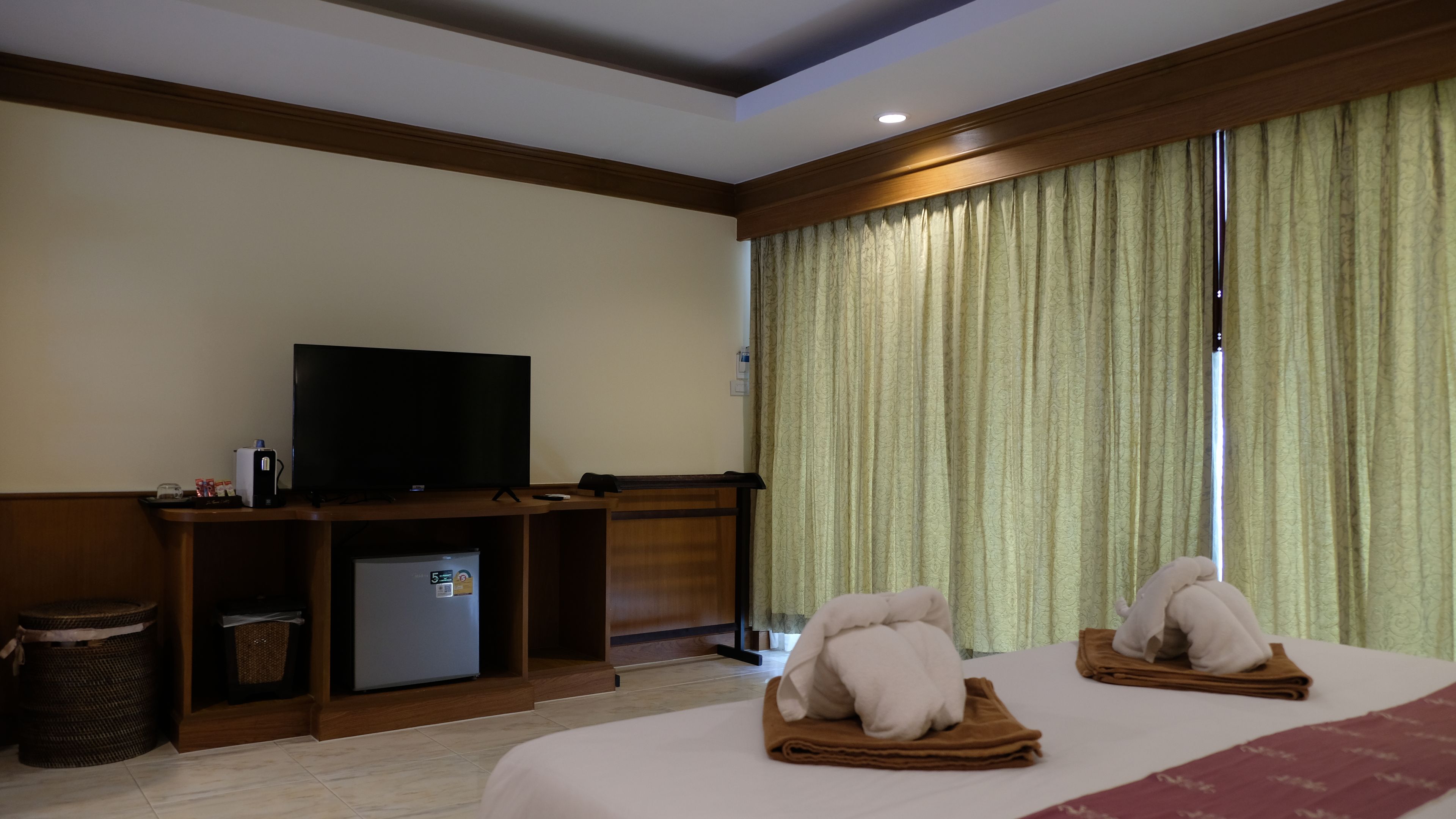 Una habitación de hotel con cama, televisión, un refrigerador pequeño y una ventana con cortinas.