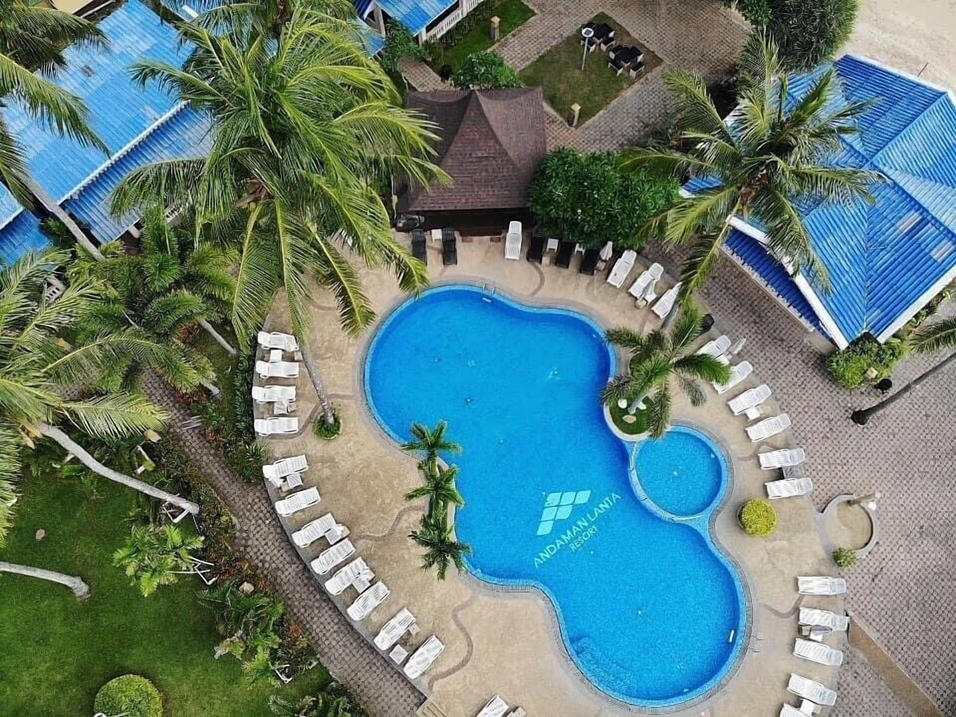 A resort with a central swimming pool surrounded by lounge chairs and palm trees.
