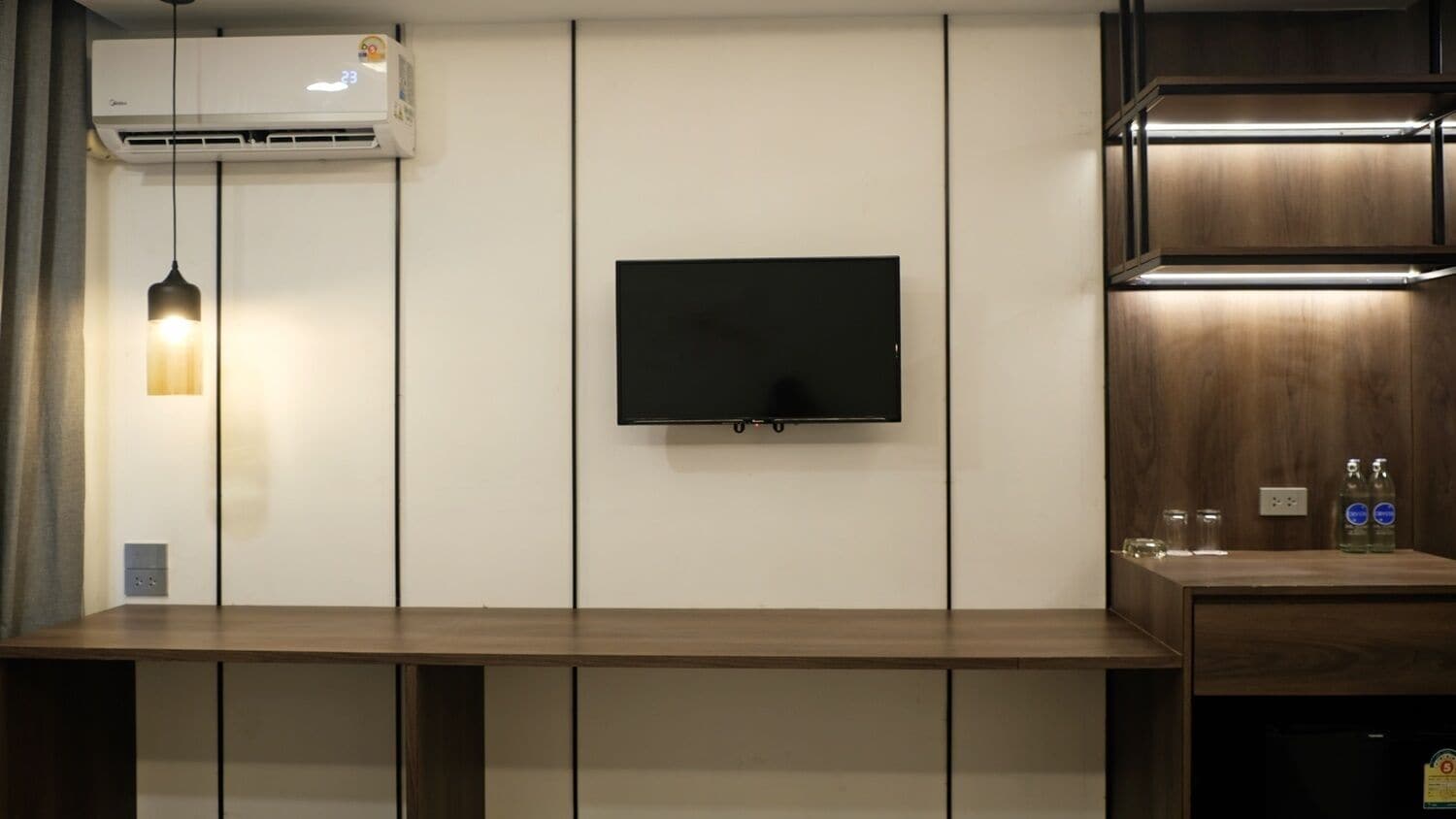 A modern living room with a flat-screen TV mounted on the wall, a wooden table, and a built-in shelf with bottles.