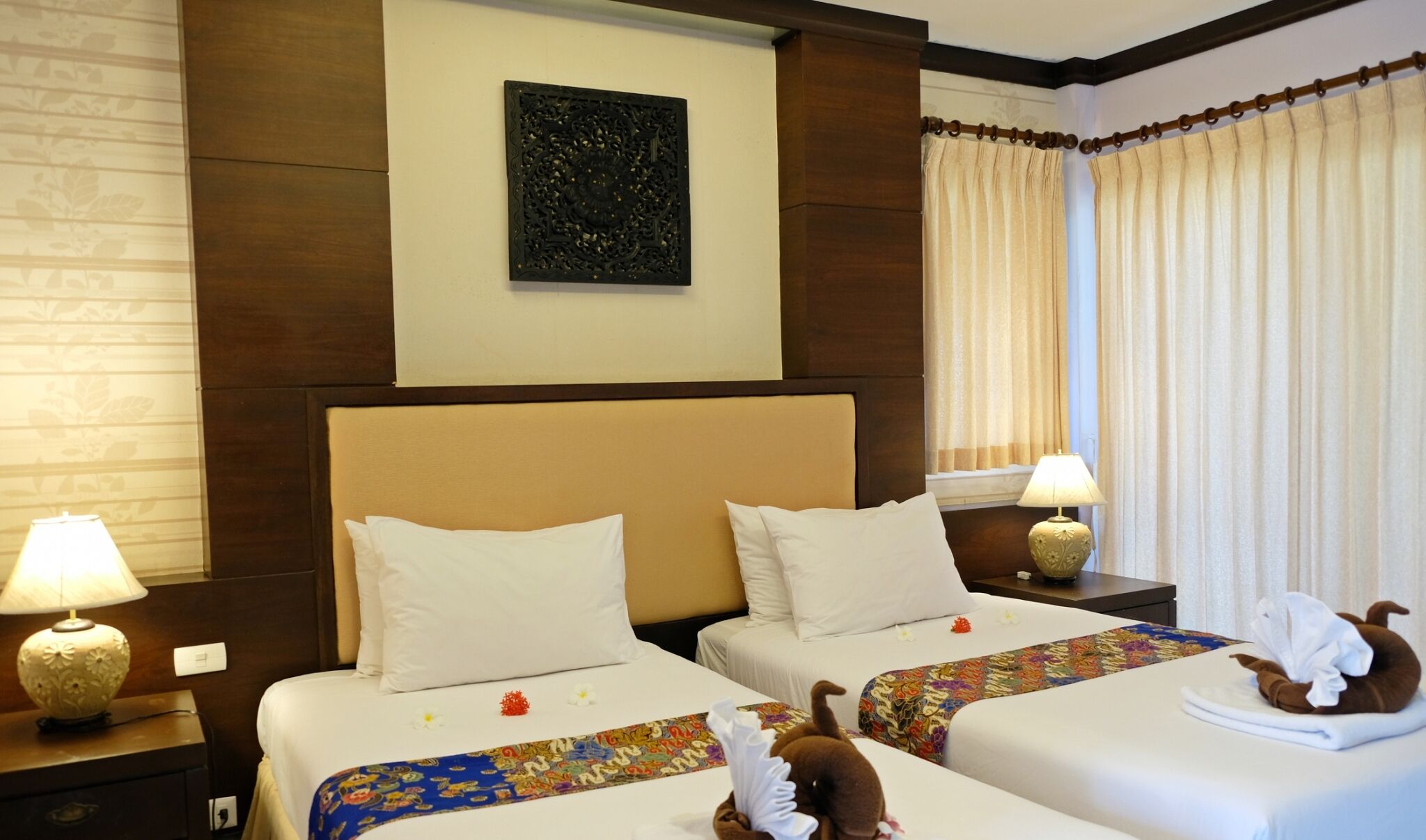 A hotel room with two beds, a decorative wall piece, and curtains.