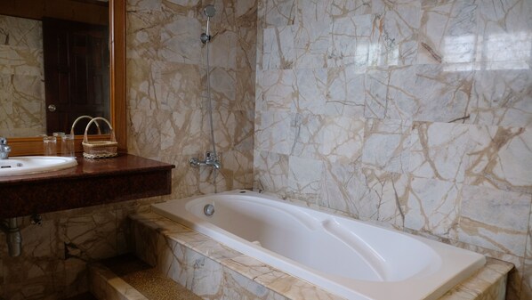 A bathroom with a marble wall, a bathtub, a sink with a mirror, and a shower.